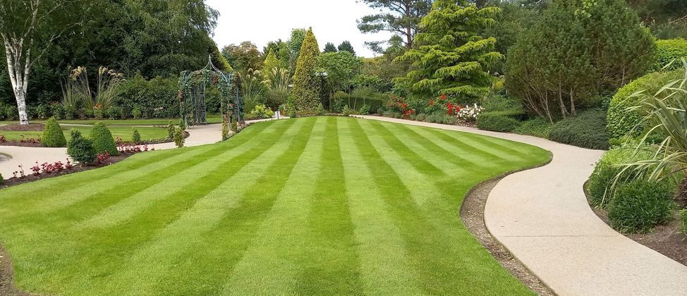 Well-manicured lawn with striped patterns, curving gravel path through a lush garden.
