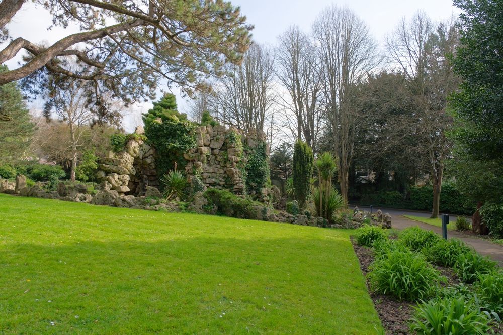 Green lawn slopes up towards a rock garden with trees; a path runs along the right side.