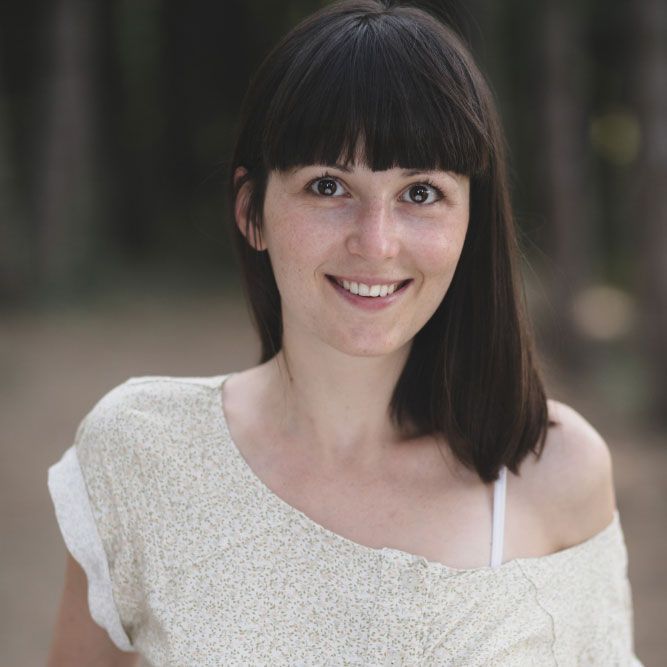 A woman with bangs is smiling for the camera while wearing a white shirt.