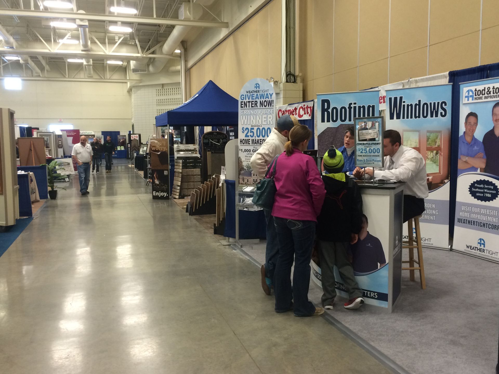 A group of people standing in front of a booth that says roofing windows