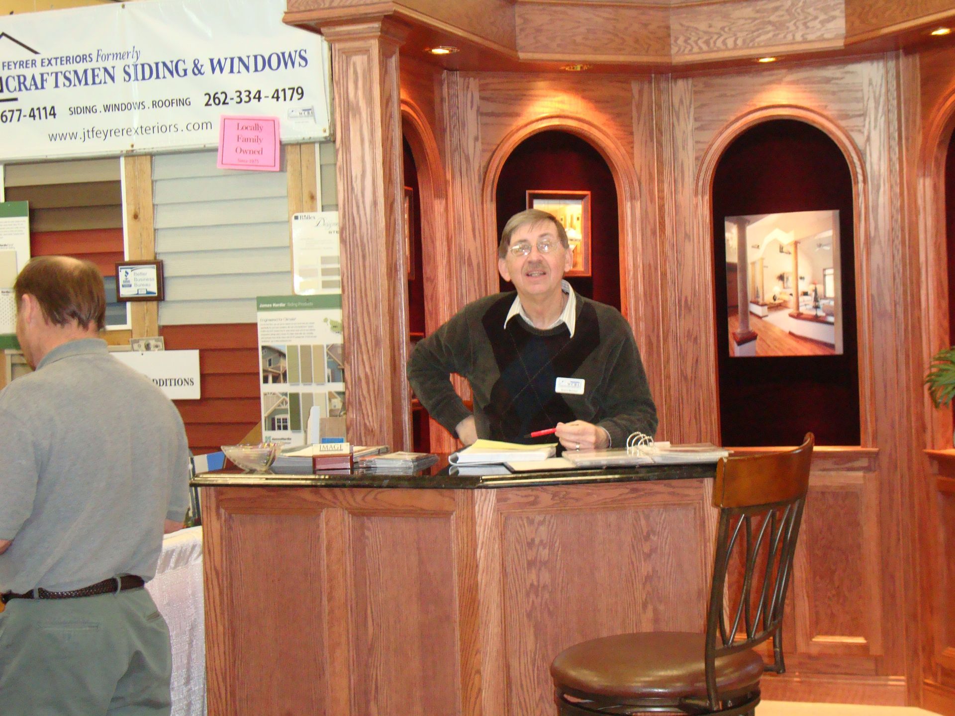 A man stands at a counter in front of a sign that says craftsmen siding & windows