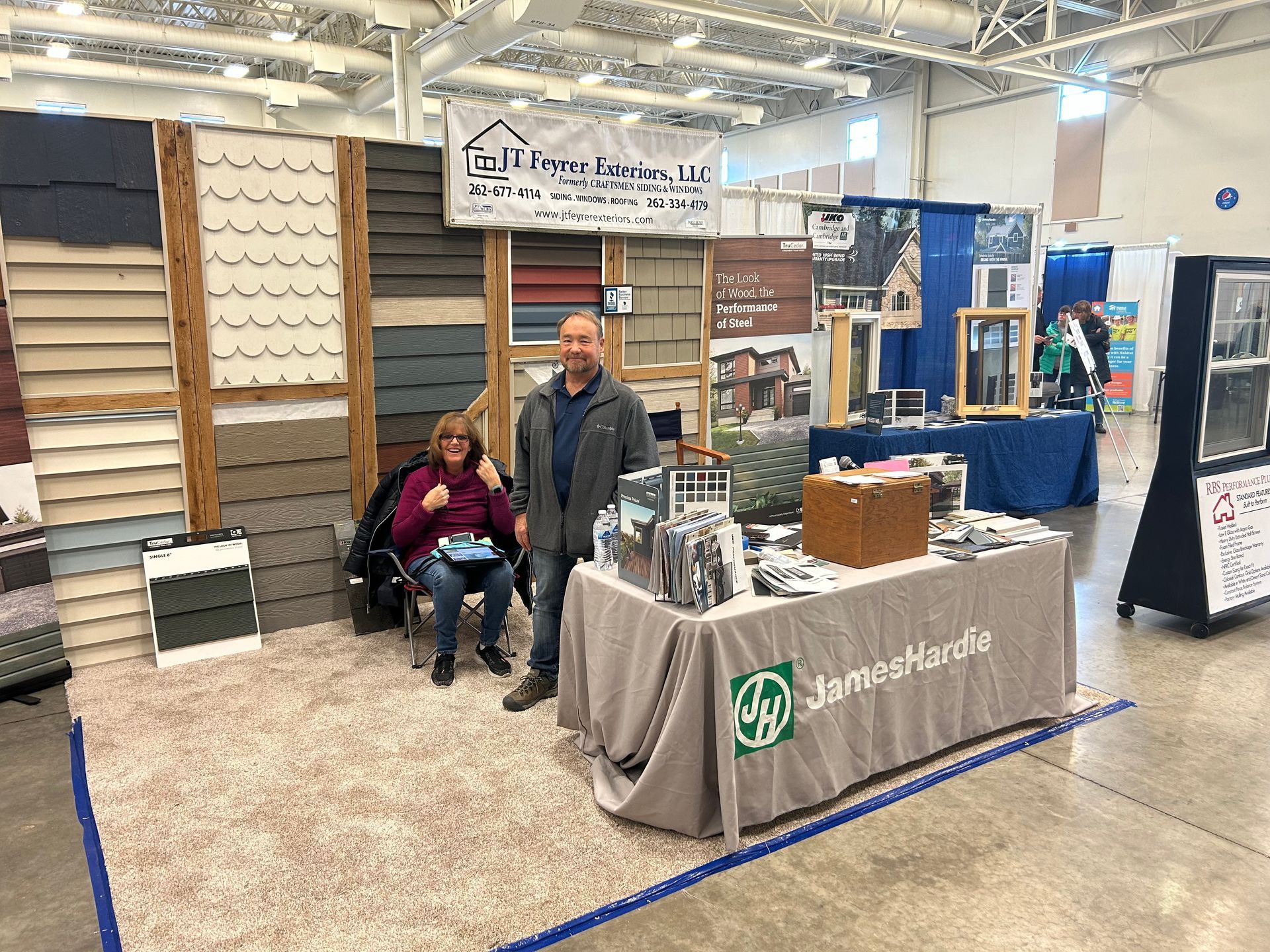 A man and a woman are standing in front of a table at a trade show.
