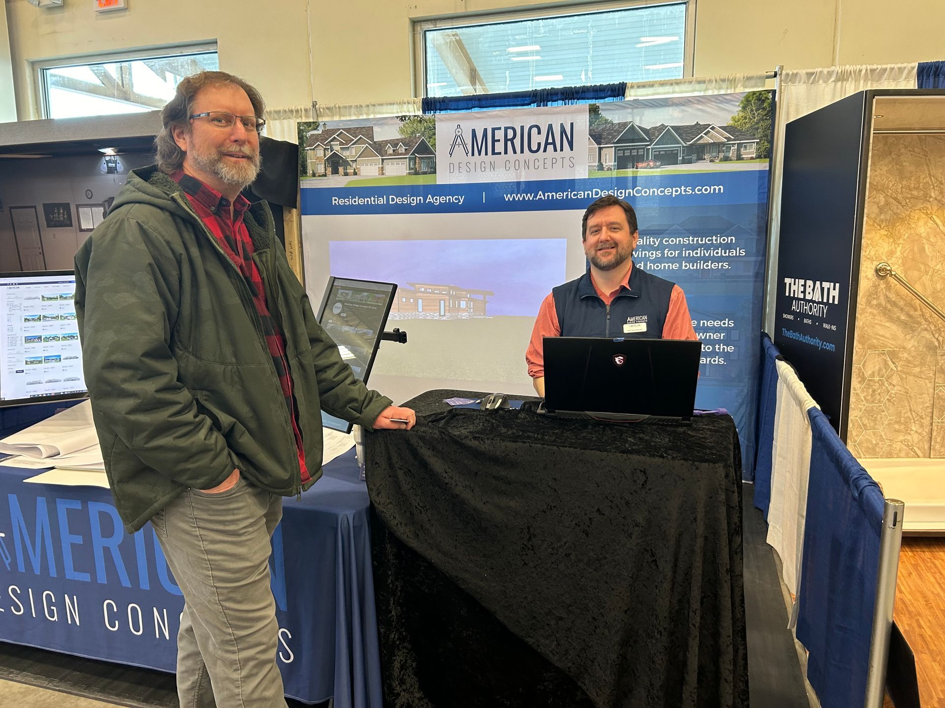 Two men are standing in front of a table with a laptop on it.