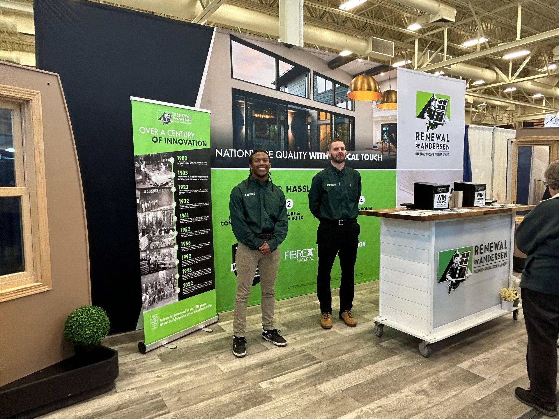 Two men are standing in front of a counter at a convention.