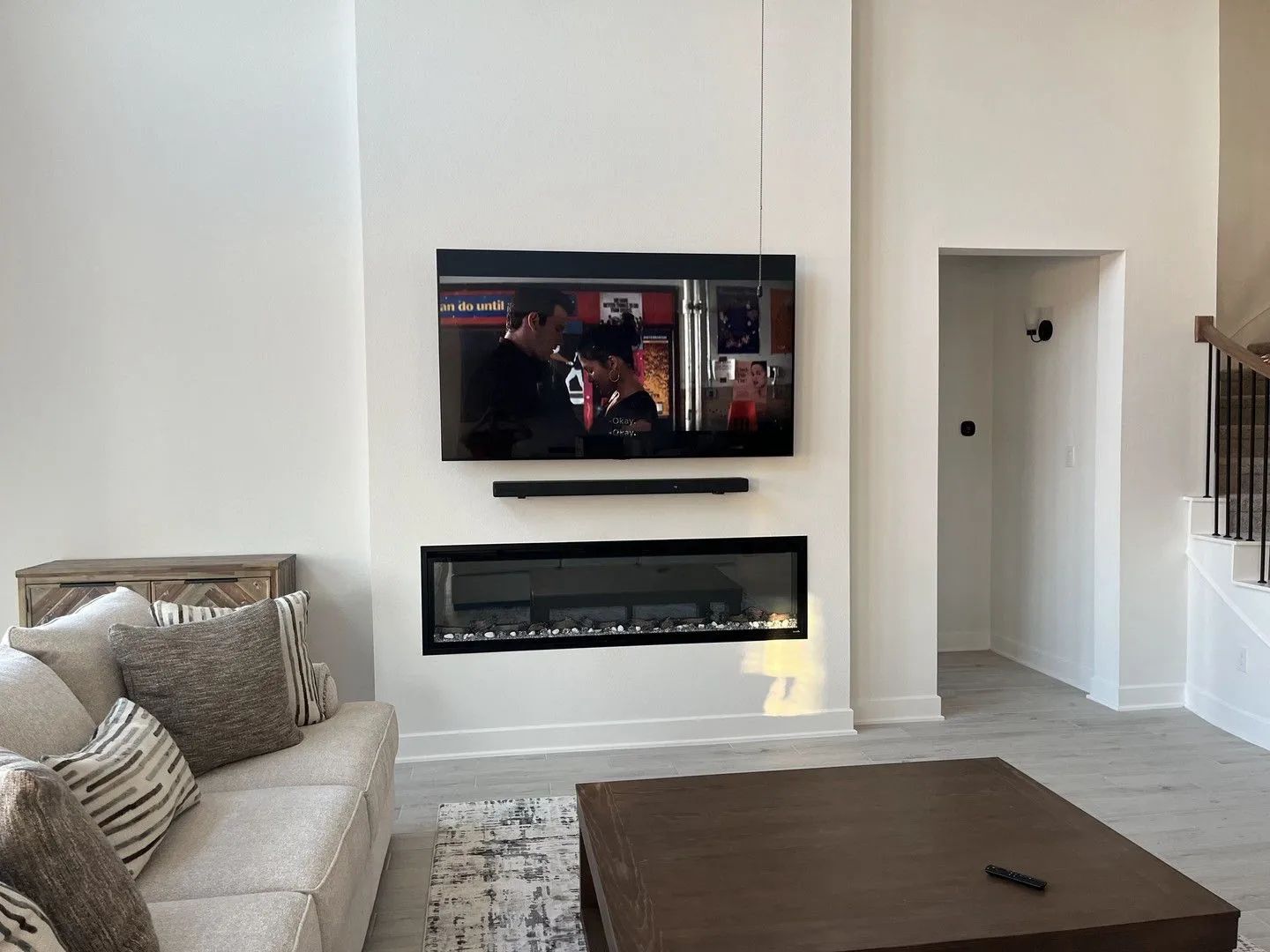 Modern living room with beige sofa, wall-mounted TV above electric fireplace, and a wooden coffee table