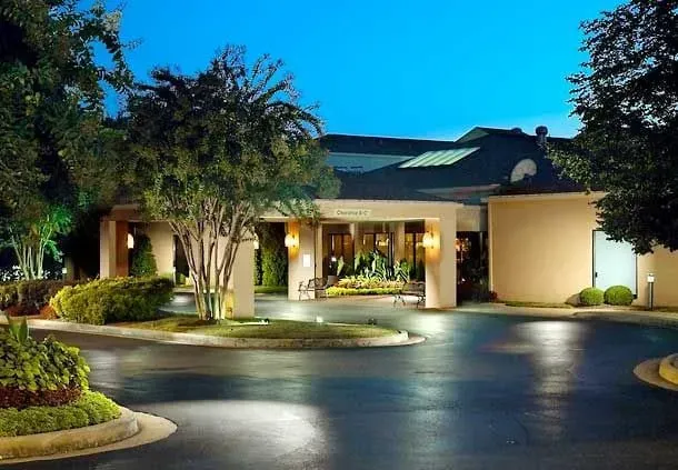 Hotel exterior with pool and lounge chairs. Blue sky overhead.