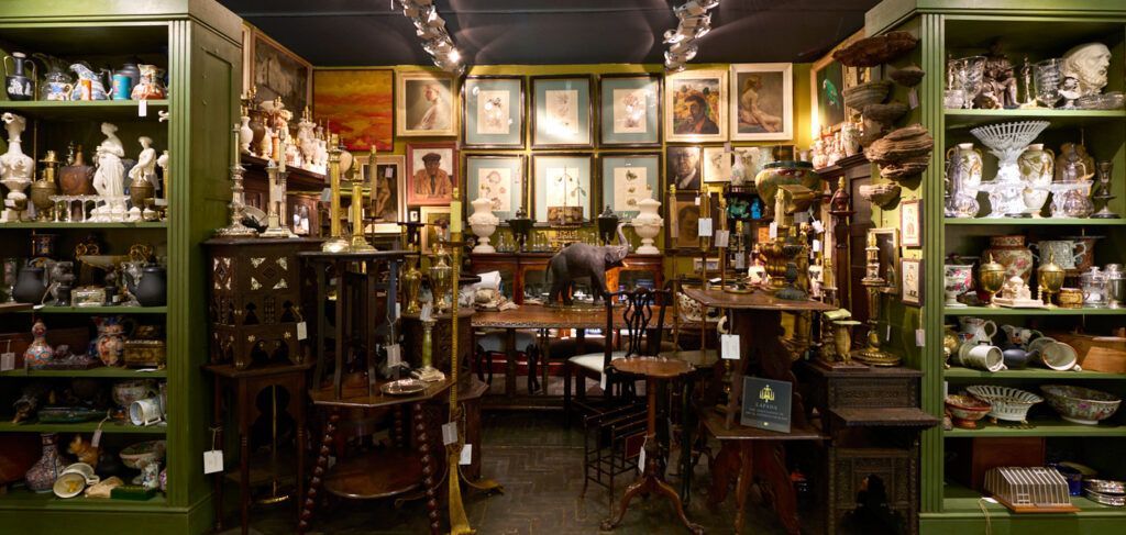 Antique shop interior filled with furniture, art, and various collectibles displayed on shelves and walls.