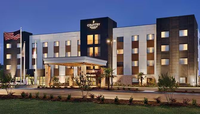 Hotel exterior with pool and lounge chairs. Blue sky overhead.