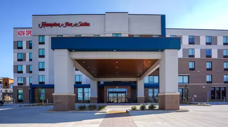 Hotel exterior with pool and lounge chairs. Blue sky overhead.