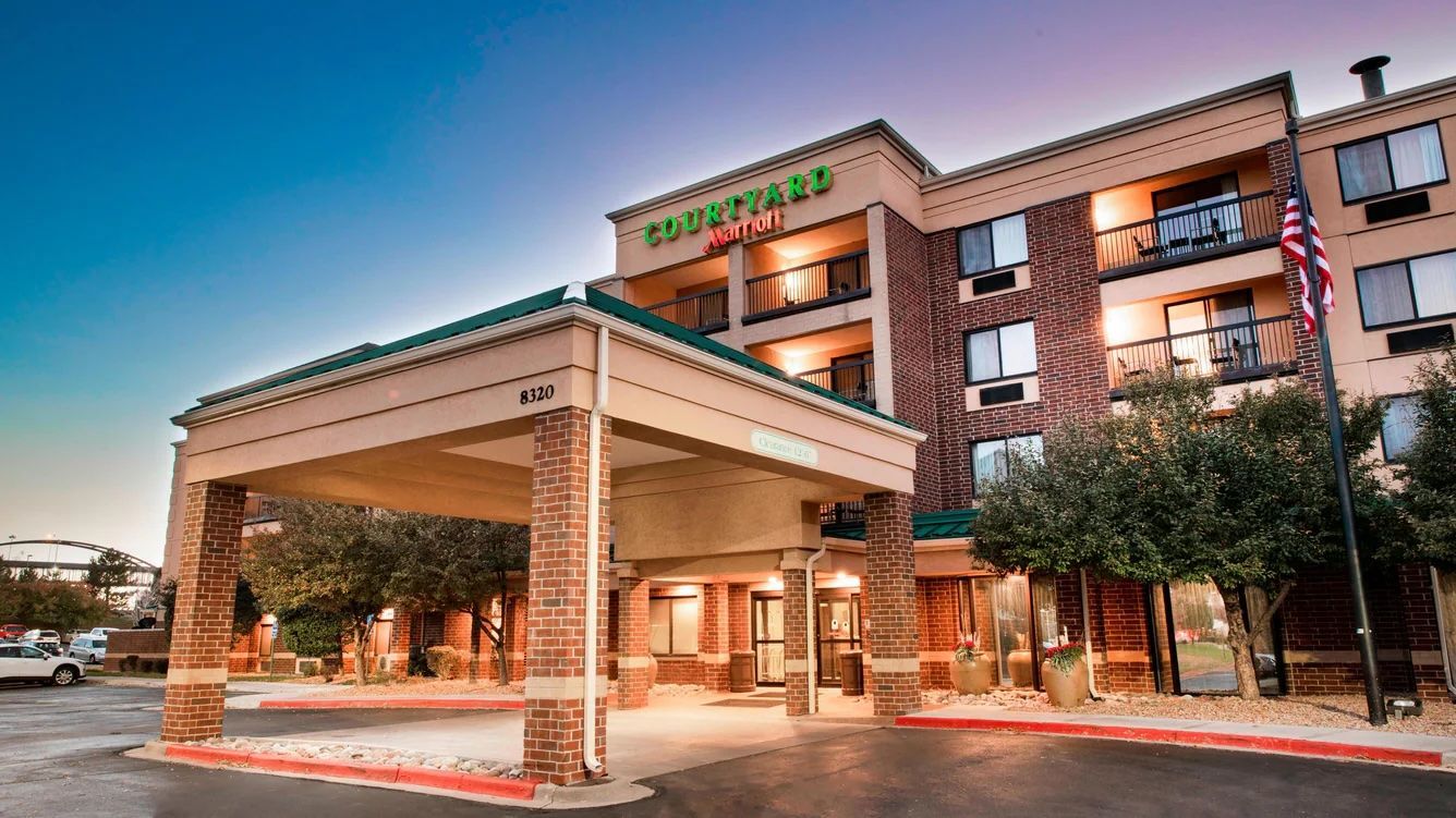 Hotel exterior with pool and lounge chairs. Blue sky overhead.