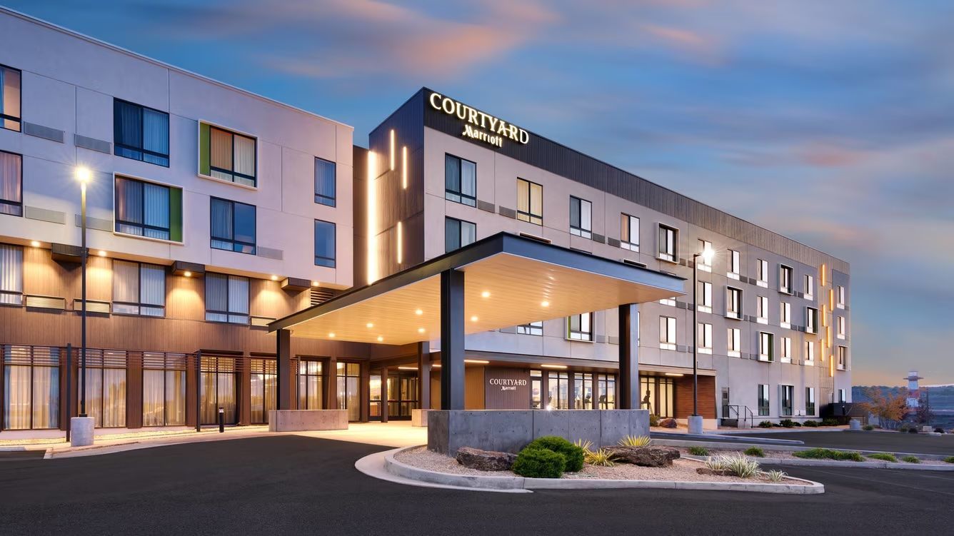 Hotel exterior with pool and lounge chairs. Blue sky overhead.