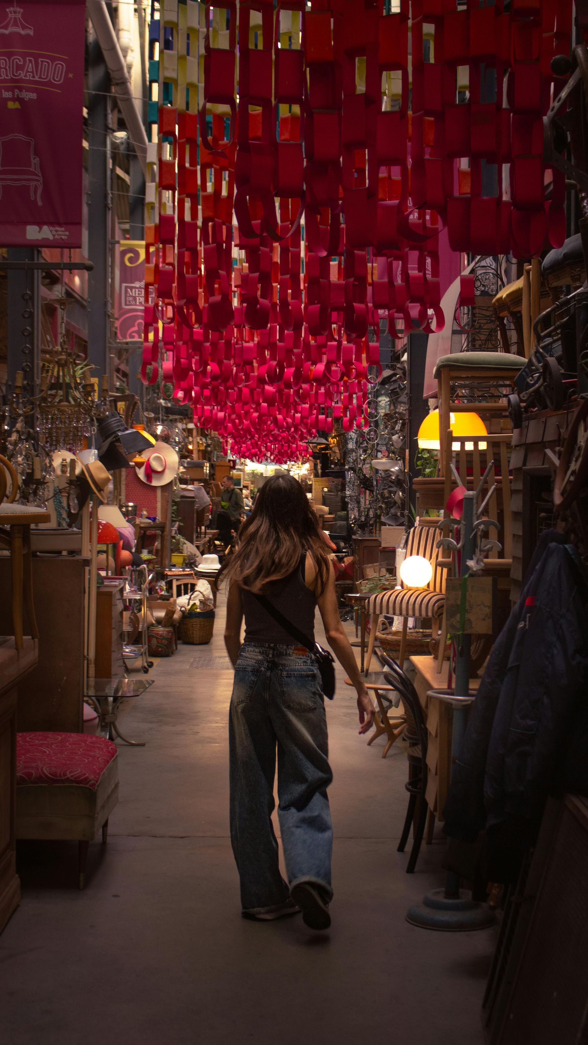 Woman walking in a shop with hanging red decorations. Shelves filled with items line the walls.