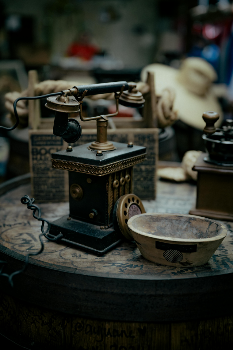Antique telephone on wooden surface with bowl and grinder in background.