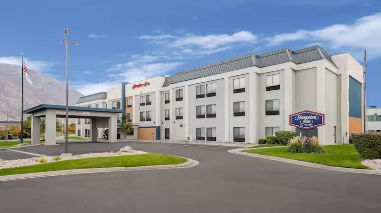 Hotel exterior with pool and lounge chairs. Blue sky overhead.