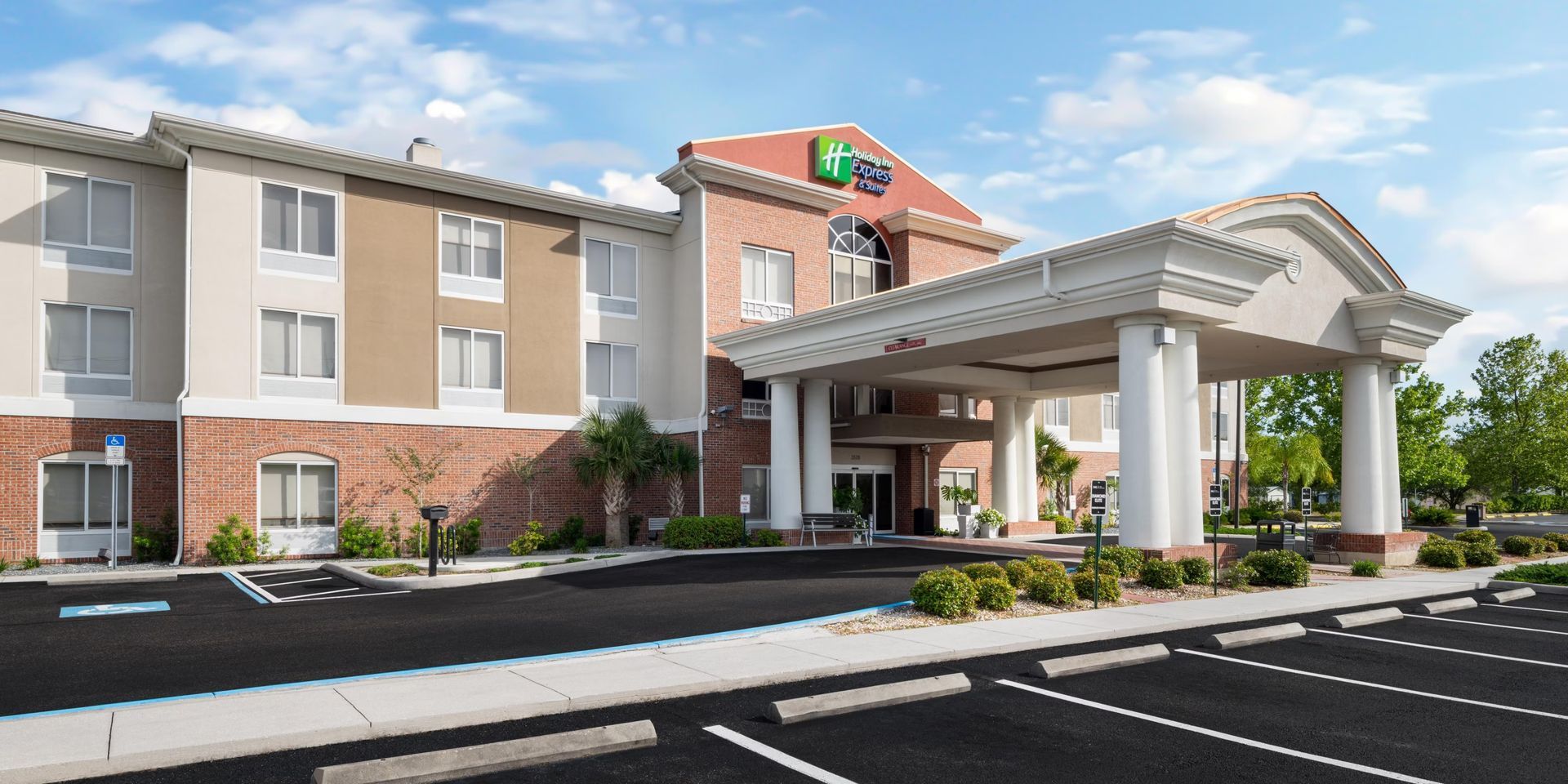 Hotel exterior with pool and lounge chairs. Blue sky overhead.
