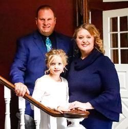 Family of three posing on a staircase, man in blue suit, woman in blue dress, child in white.