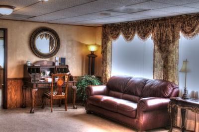 A classic living room with a desk, leather couch, curtains, and a large round mirror.