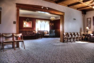 Empty room with chairs, a couch, and an archway leading to another room; carpet flooring and a chandelier.