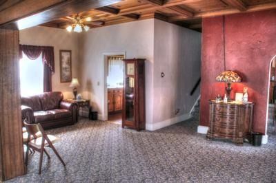 Living room with red wall and staircase, brown couch, wooden ceiling, and floral carpet.