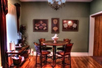 Dining area with round table, chairs, artwork on green wall, and wooden floor.