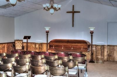 Funeral home interior with a casket, rows of chairs, and a cross on the wall.