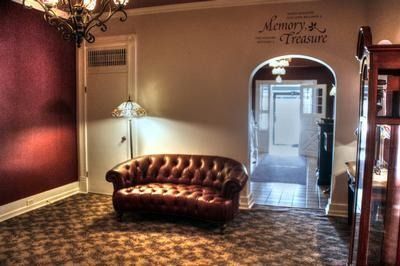 A burgundy tufted leather sofa in a room with a decorative chandelier, archway, and floral carpet.