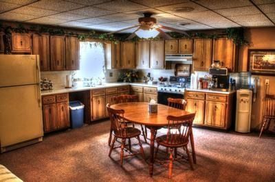 Cozy kitchen with wooden cabinets, a round table, chairs, and a ceiling fan; a refrigerator and water dispenser.