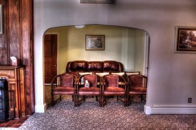 A waiting room with chairs and a couch under an archway, warm colors, carpeted floor.
