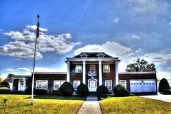 Large brick house with white columns, flag, and blue sky.