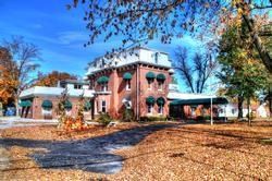 Brick building with green awnings, driveway, and fall foliage against a blue sky.