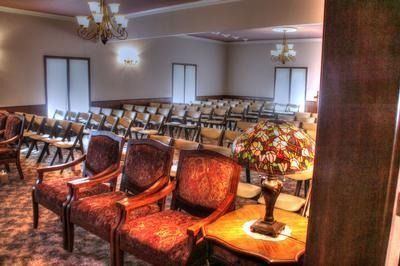 Interior of a room with rows of chairs, chandeliers, and decorative furniture.