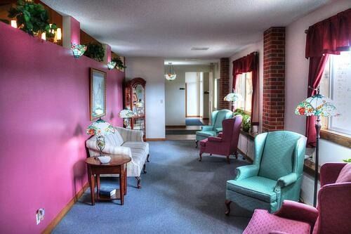 Long hallway in a building with pink and brick walls, chairs, and windows with red curtains.