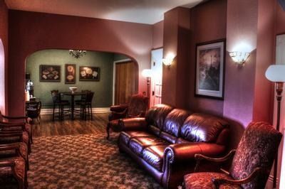 A waiting room with burgundy walls, leather sofa, patterned chairs, and an archway to a dining area with a table and chairs.