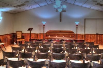 Interior of a funeral home with rows of chairs facing a closed casket and a wooden cross.
