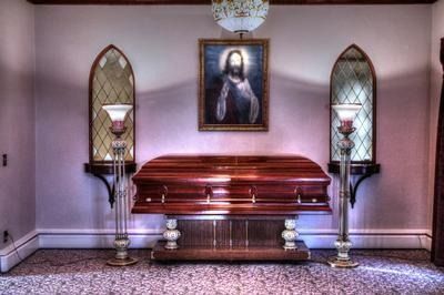 Interior of a funeral home with a closed casket, portrait, and stained-glass windows.