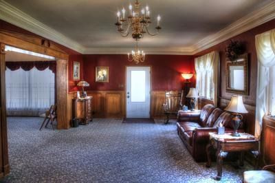 Formal living room with red walls, wood trim, chandelier, leather sofa, and patterned carpet.