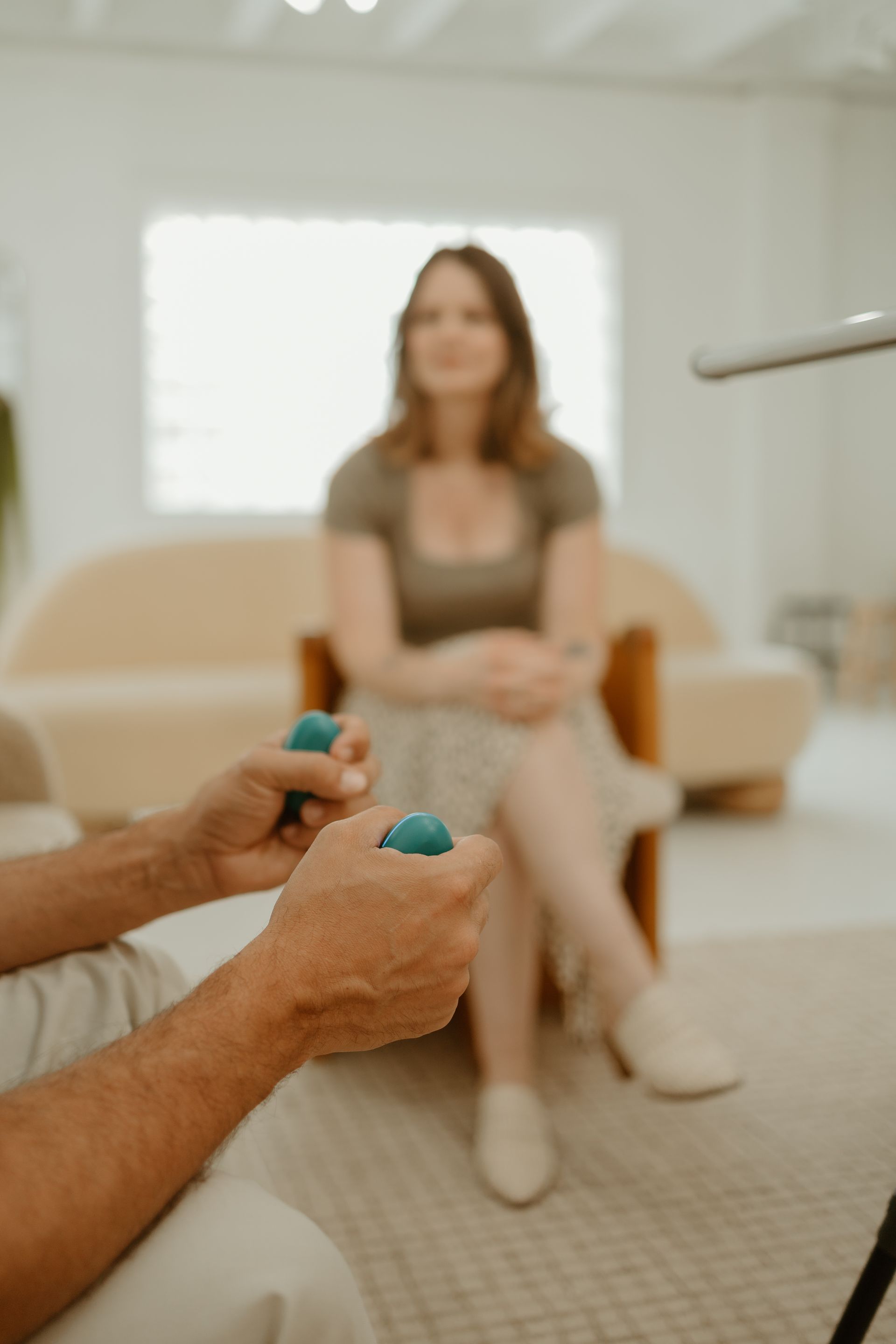 Hands holding turquoise gaming pieces in front of a seated woman in a bright room