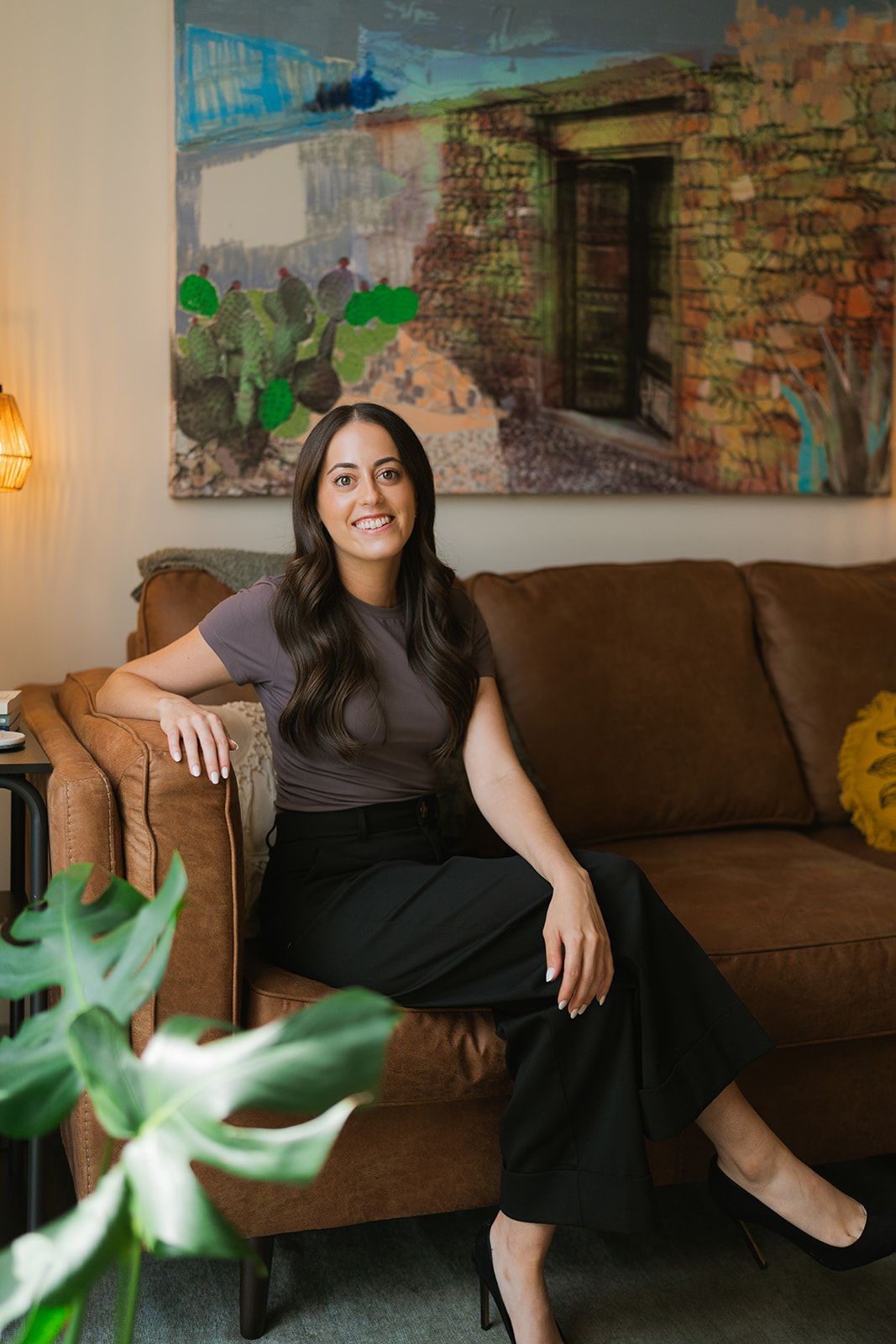 Woman sitting on a brown couch in a living room with a colorful abstract wall painting.