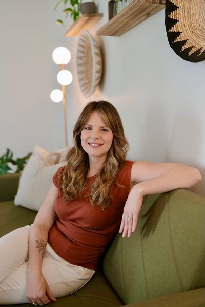 Woman in a rust top smiling on a green couch in a cozy, plant-filled room