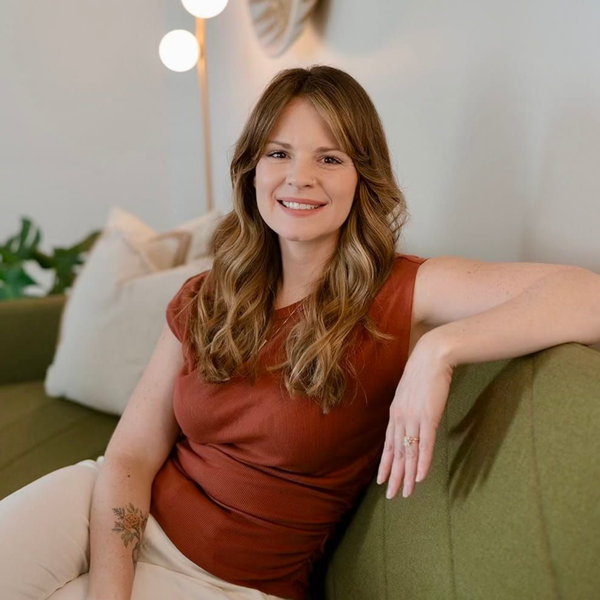 Woman in a rust top smiling on a green couch in a cozy, plant-filled room