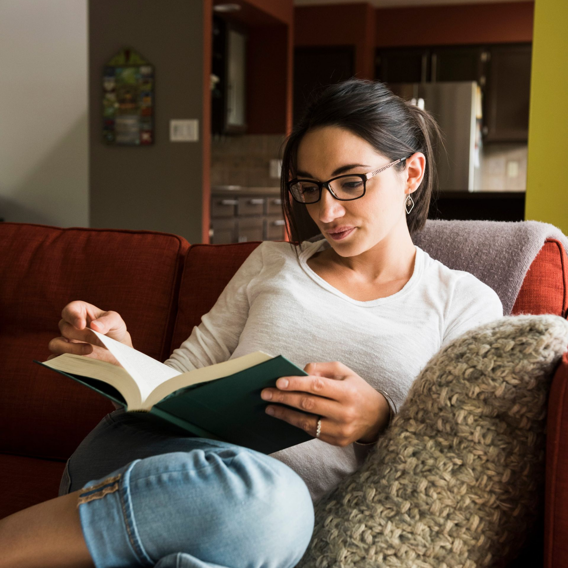 Woman reading a book on a couch with a pillow in a cozy living room