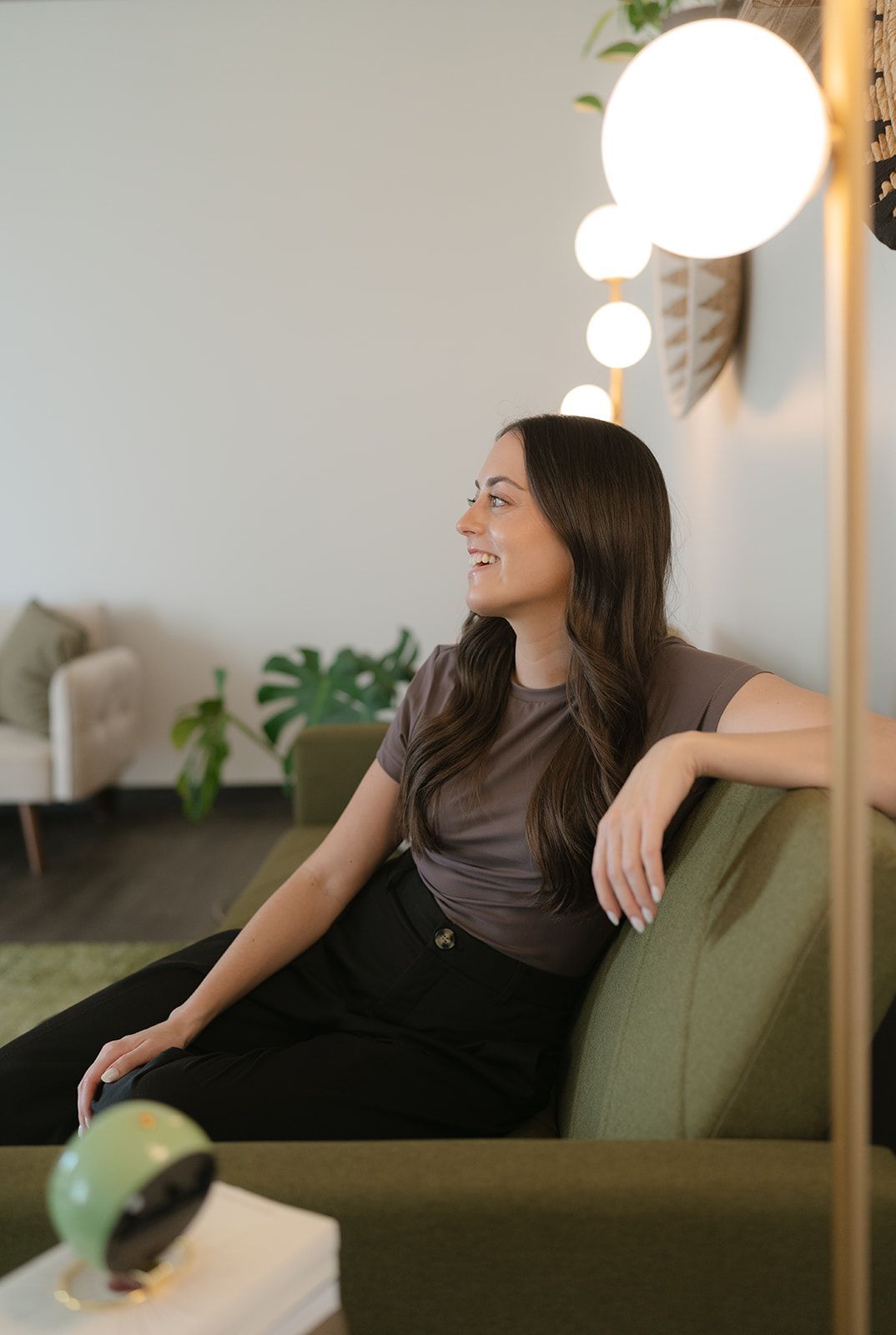 Woman sitting on a green couch, smiling and looking left in a bright modern living room