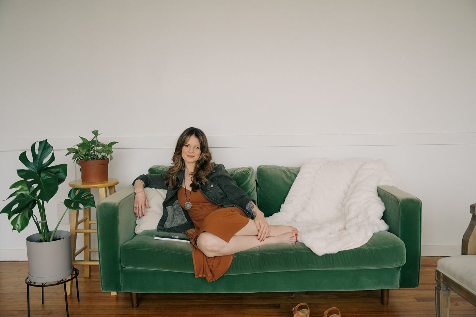Woman lounging on a green velvet sofa with a blanket in a bright living room