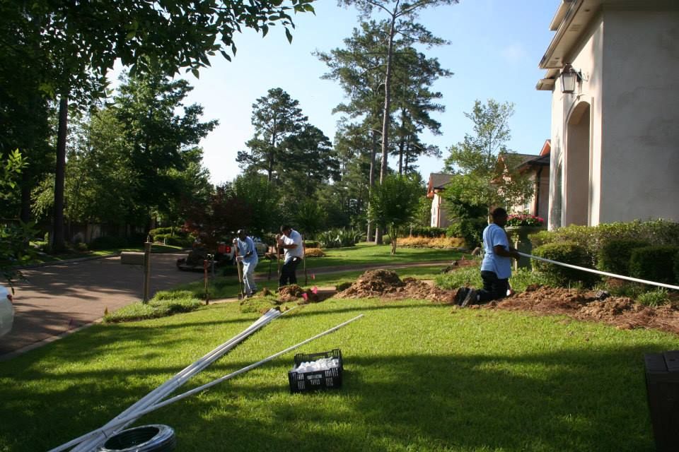 Three workers landscaping a residential lawn, installing pipes and garden beds near a house.