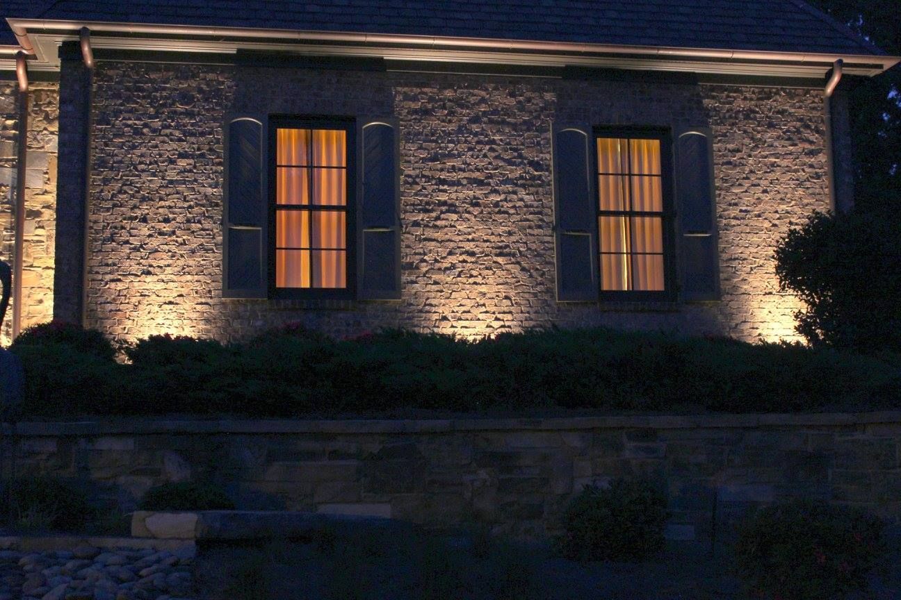 An evening view of a stone-walled house exterior with warm lighting illuminating the windows and facade.
