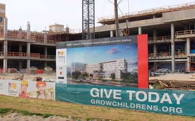 A large construction site for Children's Hospital featuring a project rendering sign and a Give Today banner.