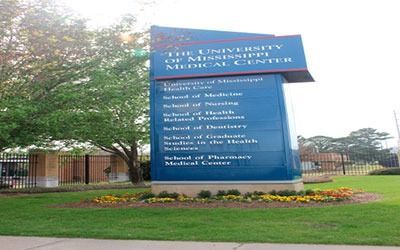 A blue signage pillar for the University of Mississippi Medical Center, set against trees and a grassy lawn.