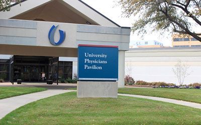 A sign reading University Physicians Pavilion in front of a medical building entrance with a blue logo.