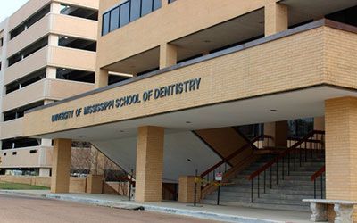A tan brick building with the sign University of Mississippi School of Dentistry over its outdoor staircase.