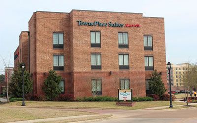 A three-story brick TownePlace Suites by Marriott hotel with a sign in front and surrounding landscaping.
